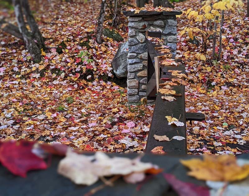 metal gate and stone pillar covered in leaves, leaves on ground nearby