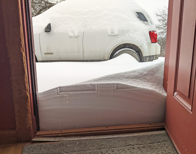 snow piled against doorway and one top of car