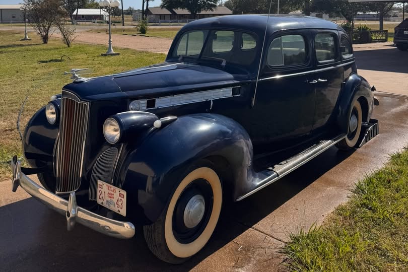 Classic 1930s vintage car in navy blue color parked on a driveway with grassy areas nearby.